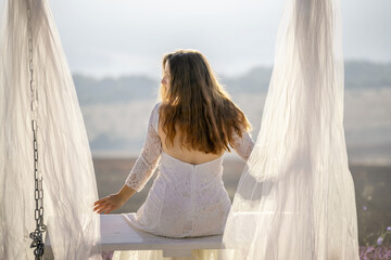 Canvas Print - A woman in a white dress sits on a bench under a white canopy. The scene is serene and peaceful, with the woman looking out over the landscape.