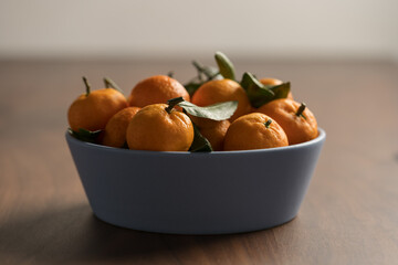 Wall Mural - Small organic tangerines with leaves in ceramic bowl on wood table