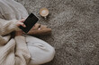 © Floral Deco - Woman sitting on fluffy carpet with cup of coffee and using mobile phone. Cozy morning routine concept