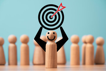 Wooden miniature figure smile and holding dartboard with arrow in front of many figures for leadership and business target concept.