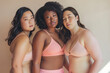© Natalia - Women of different ethnicities and body types standing in front of a beige background hugging one another. Unity, participation, diversity, multicultural society. Women power.