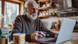 © amila - Elderly Bearded Man Enjoying Black Friday Online Shopping | Joyful Senior Male Using Laptop and Credit Card for E-Commerce Purchases at Home