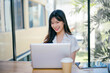 © Parichat - Young Professional Woman Working on Laptop in Modern Office with Natural Light and Greenery in the Background