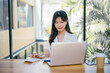 © Parichat - Young Professional Woman Working on Laptop in Modern Office with Natural Light and Greenery in the Background