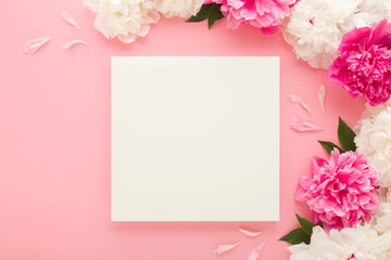 Wall Mural - Fresh beautiful soft peony flowers with green leaves and blank white greeting card on light pink table background. Pastel color. Closeup. Empty place for lovely text, quote or sayings. Top down view.