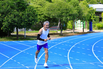 Senior Asian athlete is practicing running in the professional blue track for professional exercise, sport training workout and healthy for longevity