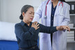 © amnaj - Elderly woman receiving medical care from a doctor, experiencing shoulder pain, physical examination in a clinical setting.