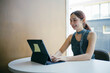 © Parichat - Young Woman Working on a Tablet at a Modern Office Desk, Smiling and Engaged in Her Task, Wearing a Stylish Sleeveless Top, with a Minimalist Background and Natural Light from a Window