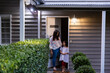 © Austockphoto - A woman and a child standing outside the front porch of a weatherboard house at night