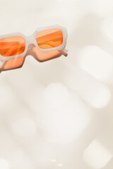 Wall Mural - Top view trendy transparent peach orange colored sunglasses on beige background, shadow and glare at sunlight, summer fashion plastic-framed eyeglasses. Summer rest concept, copy space