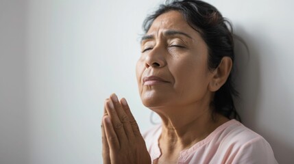 Wall Mural - A woman with closed eyes hands clasped in prayer leaning against a wall with a soft expression of contemplation or sadness.
