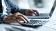 © iuricazac - A person's hand operating a calculator while sitting at a desk with a laptop.