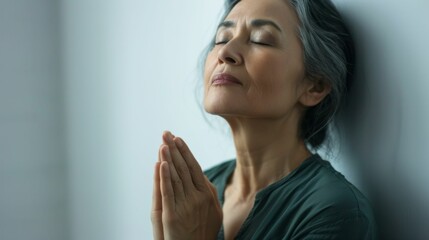 Wall Mural - A woman with closed eyes hands clasped together in prayer leaning against a wall with a serene expression.