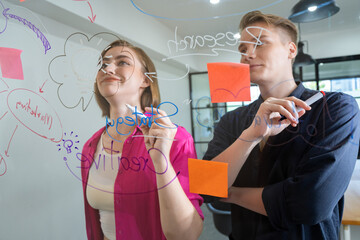 Wall Mural - Couple of young creative start up business people brainstorming idea and solving problems by using sticky note and mind map at glass board, meeting room. discussing, working together. Immaculate.