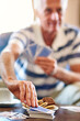 © peopleimages.com - Elderly man, table and hand with playing cards at home for fun competition, activity and strategy. Relax, senior person and snack with picking in game for challenge, contest and problem solving