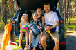 © ronstik - happy family with kids sitting in car trunk with camping supplies at natural park. summer vacation travel, road trip