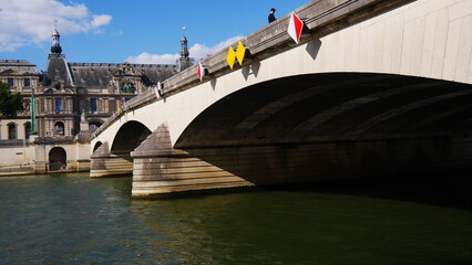 Gros plan d'un grand pont de pierre historique de Paris et de la Seine, sous un beau, jeu d'ombre et de lumière de soleil, fleuve vert, panneaux de signalisation de bateaux, direction, sous ciel bleu