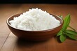 © juliars - Freshly cooked white rice served in a rustic wooden bowl with green basil leaves on a wooden table