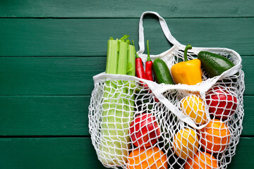 String bag with different vegetables on green wooden table, top view. Space for text