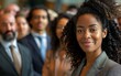 © imagineRbc - A woman with curly hair is smiling at the camera. She is surrounded by other people, some of whom are wearing ties. Concept of professionalism and confidence, as the woman stands out among the crowd