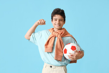 Wall Mural - Teenage boy with soccer ball showing muscles on blue background