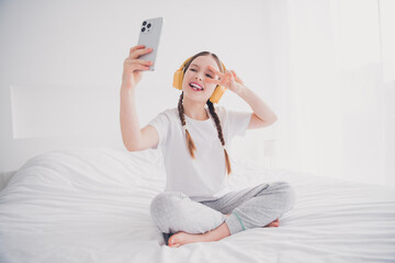 Poster - Portrait of cute adorable lovely girl sitting bed recording video weekend v-sign white light interior indoors