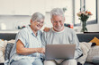 © Daniel - Pretty elderly 70s grey-haired couple resting on couch in living room hold on lap laptop watching movie smiling enjoy free time, older generation and modern wireless technology advanced users concept.