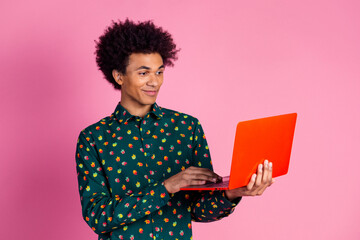 Sticker - Portrait of clever positive guy with wavy hair dressed print shirt look at laptop in hands chatting isolated on pink color background