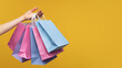 © wpadington - Studio shot of woman hand holding a bunch of colorful paper shopping bags isolated over yellow background