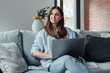 © Daniel - Concentrated millennial girl sit on couch working on laptop browsing internet at home during lazy weekend, focused young woman freelancer busy using computer surfing wireless web shopping online.
