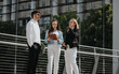 © qunica.com - Three business professionals engaged in a discussion outdoors in a modern urban environment. They are standing near a railing with buildings in the background.