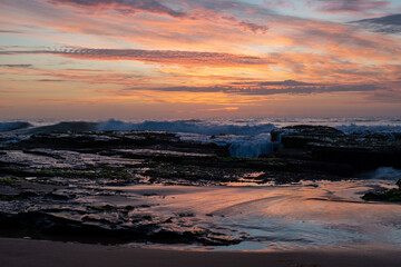 Wall Mural - Sunrise rocky breaking waves beach orange yellow clouds	