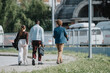 © qunica.com - Three young professionals are captured walking together along a city pathway, engaging in friendly conversation, possibly discussing work.