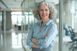 © pham - A smiling woman with gray hair stands confidently in an office building with her arms crossed