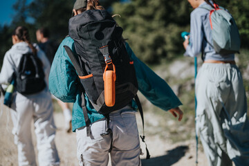 Wall Mural - Group of friends hiking on a sunny day. They carry backpacks and walk together through a scenic outdoor trail.