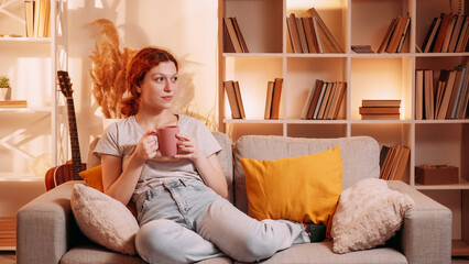 Enjoy coffee. Home leisure. Relaxed calm woman drinking mug tea beverage carefree rest daydream cozy couch warm pastel color interior free space.