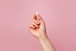 © Nastya - A hand holding a white capsule against a pink background