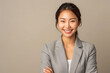 © Bank-adtapon - Smiling woman in a grey blazer with arms crossed on a beige background. Studio portrait ,generative ai