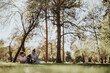 © qunica.com - A young man and woman sit on the grass, surrounded by trees, focused on a book in a peaceful park atmosphere.