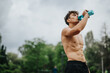 © qunica.com - Young athletic man drinking water while exercising outdoors. Staying hydrated and fit during outdoor workout under the cloudy sky.