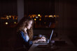 © Halfpoint - Beautiful university student is writing her thesis on a laptop at night, sitting at home at table, focusing on her research. Preparing for final exam, studying.