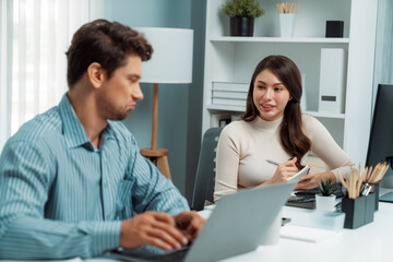 Wall Mural - Smart manager talking to woman coworker while typing on laptop asking information data research project for business analysis report on desk at side view at modern office in morning time. Postulate.