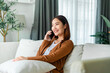 © Monster Ztudio - Happy young asian woman relax on comfortable couch at home texting messaging on smartphone, smiling girl use cellphone chatting