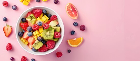 Fresh fruit salad in a bowl on a pink background from above.