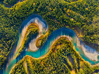 Drone view of the river in the forest. An aerial view of an woods. Winding river among the trees. Turquoise mountain water. Landscape with soft light before sunset.