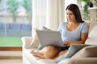 © Antonioguillem - Woman is using laptop on a couch at home