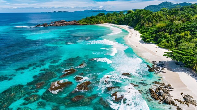 A breathtaking aerial top view of an idyllic white sand beach surrounded by lush green forests and crystal-clear turquoise waters, with gentle waves crashing against rocky outcrops, creating a serene