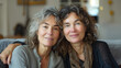 © AISTEL - two happy casual middle aged women with grey hair sitting on a sofa in a living room