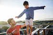 © Westend61 - Father supporting son walking on boardwalk railing with arms outstretched at beach