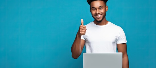 Poster - A young funny African American guy wearing a casual white t shirt stands alone on a blue background representing a lifestyle concept He points his index finger at a laptop with a blank screen allowin